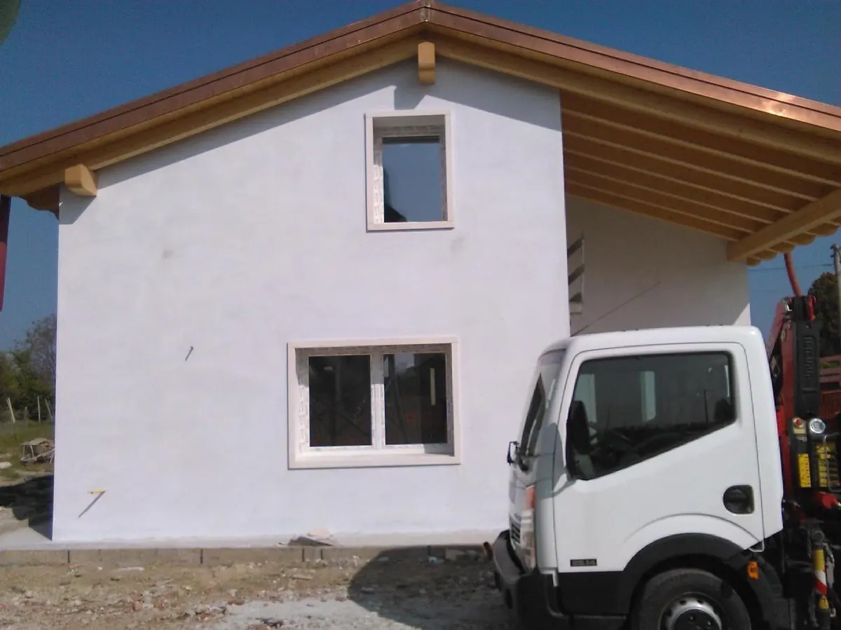 Casa bianca in costruzione con finestre appena installate e un camion con gru
