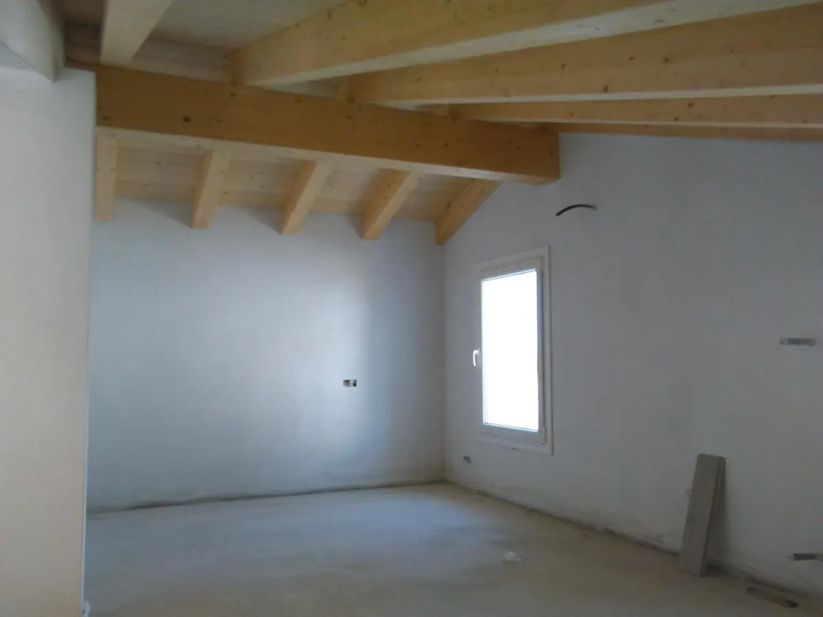 Stanza con soffitto a travi in legno, pareti intonacate e finestra installata