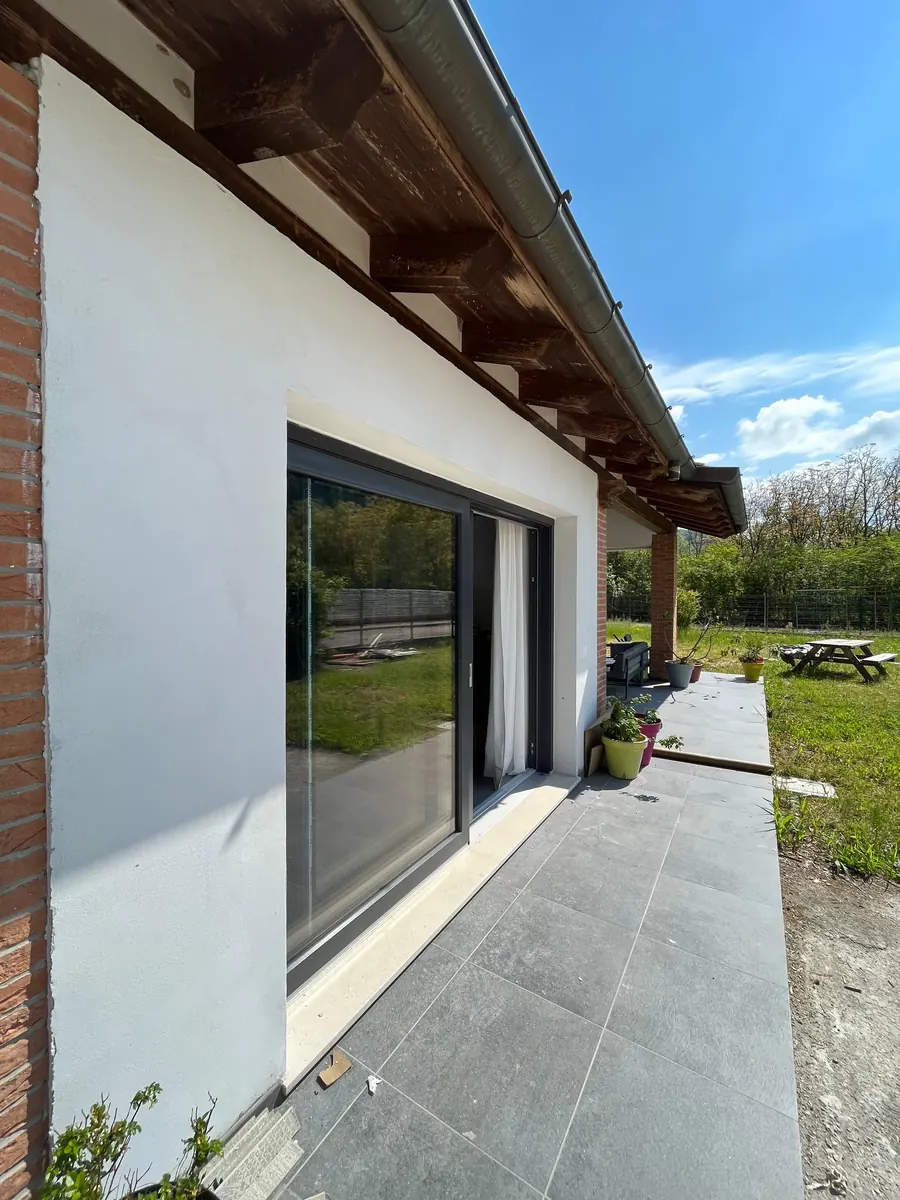 Portafinestra scorrevole a vetro con telaio scuro vista dall'esterno, su una casa con tetto in legno